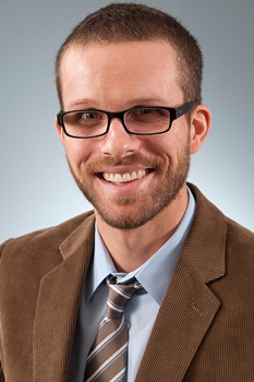 a man wearing a suit and tie smiling and looking at the camera