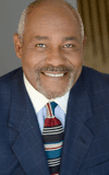 Thom Gossom Jr. wearing a suit and tie smiling at the camera Thom Gossom Jr. wearing a suit and tie smiling at the camera