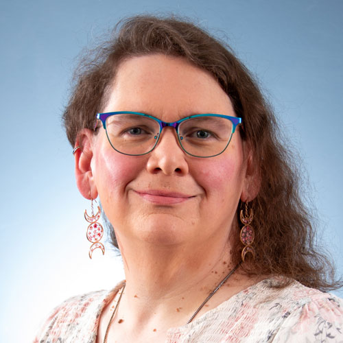 Auburn University at Montgomery faculty headshot of a smiling person with glasses and earrings on a blue background