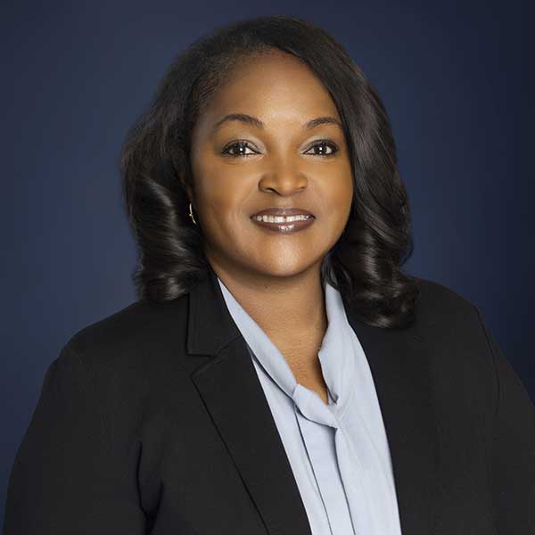 A professional woman in a blazer smiling against a dark background.