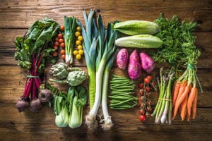 a wooden table topped with lots of fresh vegetables on a cutting board