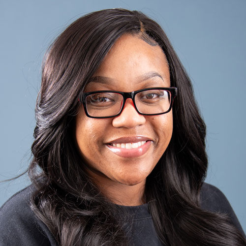 A woman with glasses smiling against a blue background.