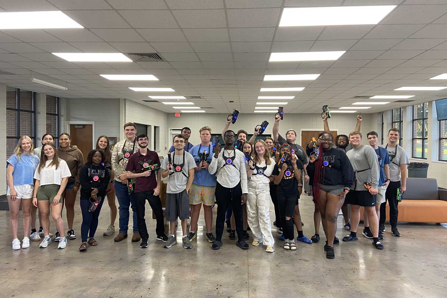 Group of students at Auburn University at Montgomery holding laser tag gear, smiling indoors.