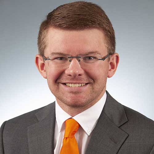 a man wearing a suit and tie smiling at the camera