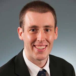 a man wearing a suit and tie smiling at the camera