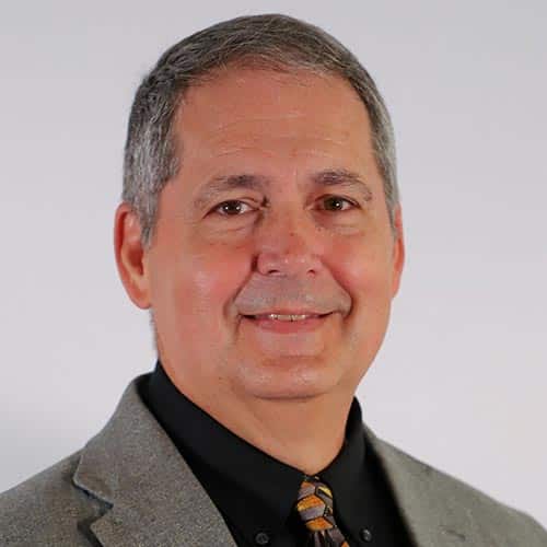 a man wearing a suit and tie smiling at the camera