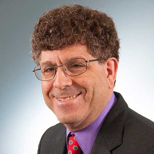 a man wearing a suit and tie smiling and looking at the camera