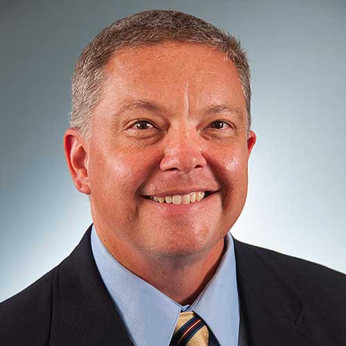 a man wearing a suit and tie smiling at the camera