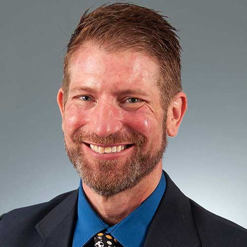 a man wearing a suit and tie smiling at the camera