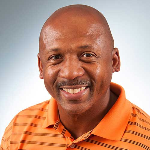 a man wearing an orange shirt smiling and looking at the camera