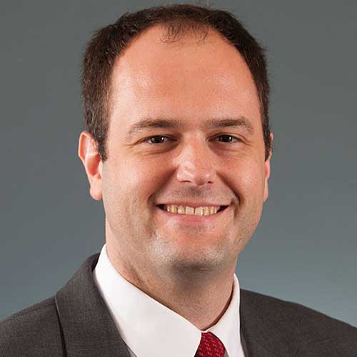 a man wearing a suit and tie smiling at the camera