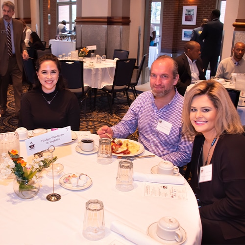 A Group Of People Sitting At A Table Posing For The Camera