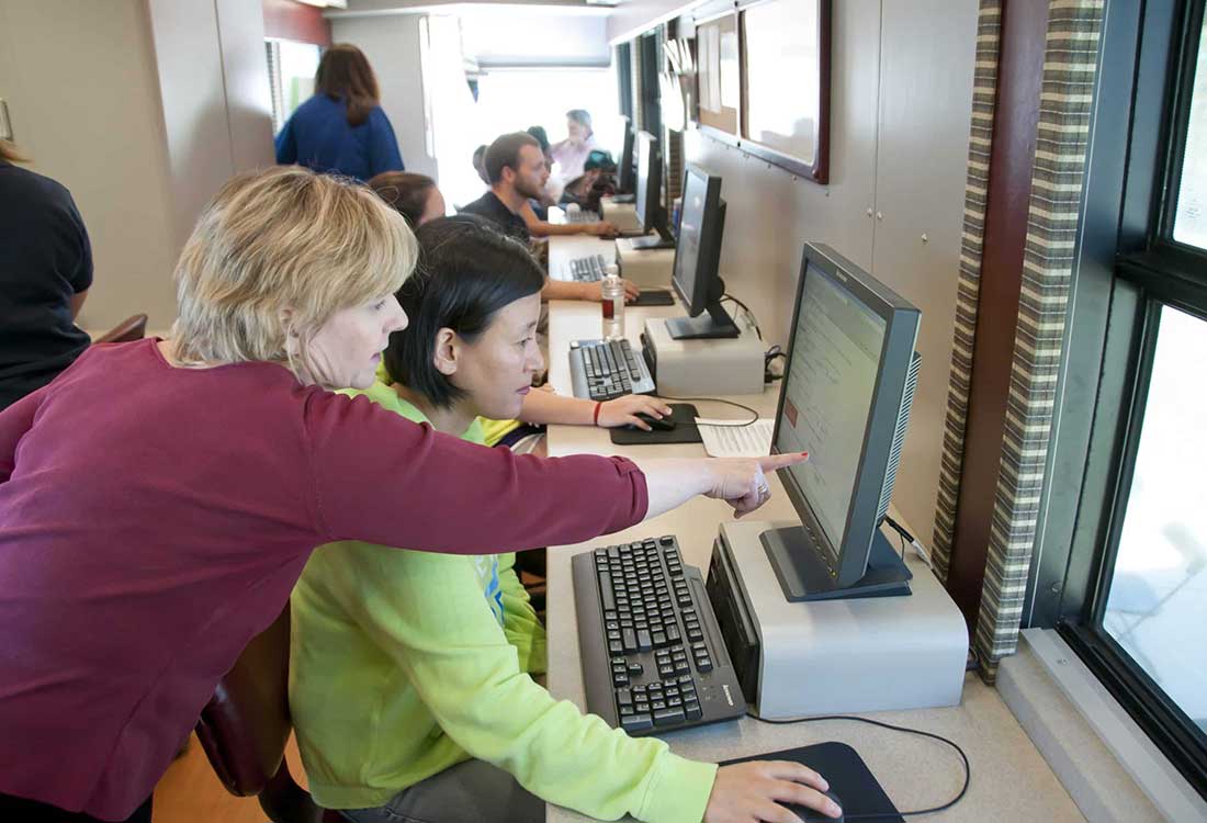 Auburn University at Montgomery instructor helps a student in a computer lab, pointing at a desktop screen