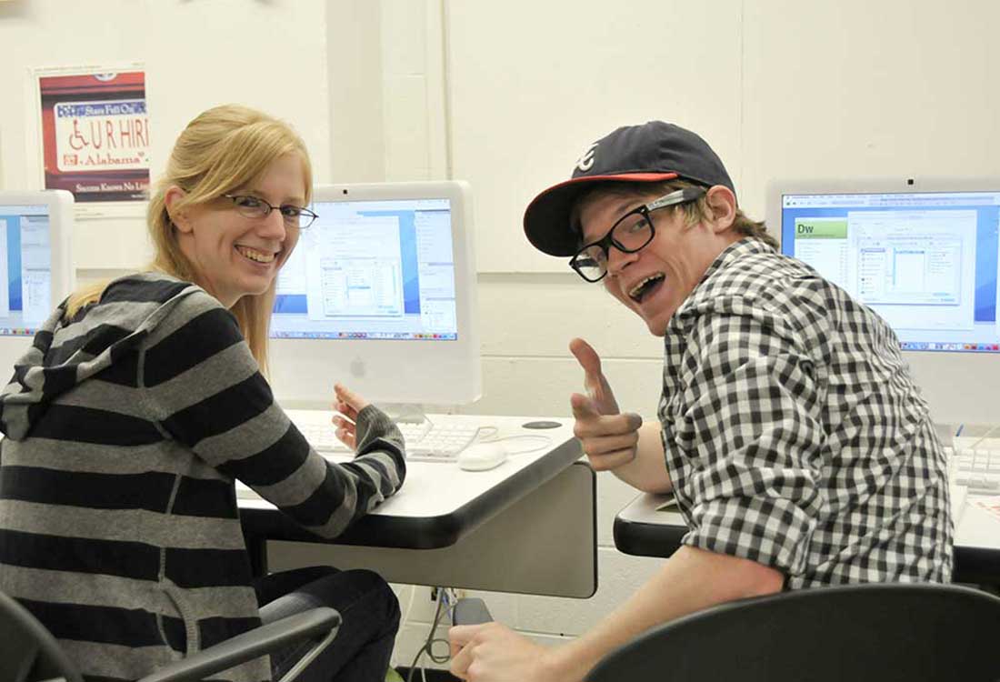 Auburn University at Montgomery students working together in a computer lab, smiling at iMac screens during a class project.