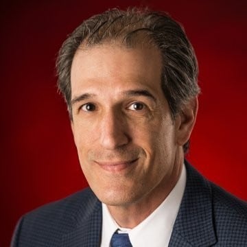 a man wearing a suit and tie smiling and looking at the camera