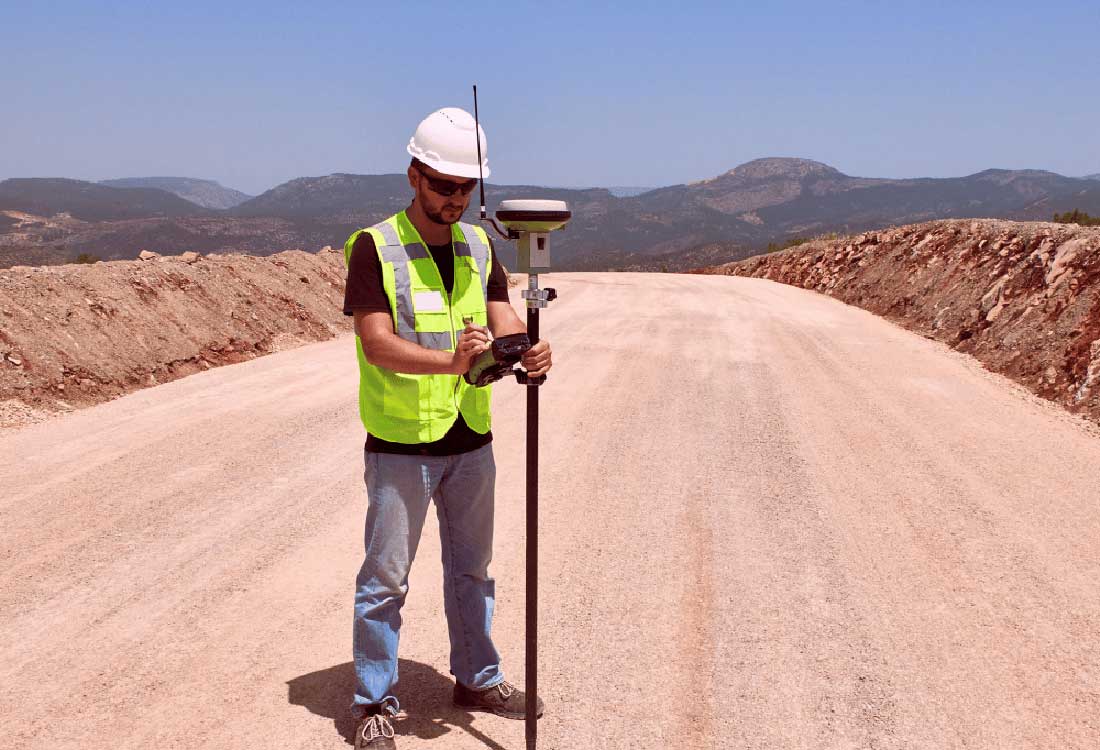 AUM civil engineering student uses GPS rover to survey a new rural road, wearing a hard hat and safety vest.