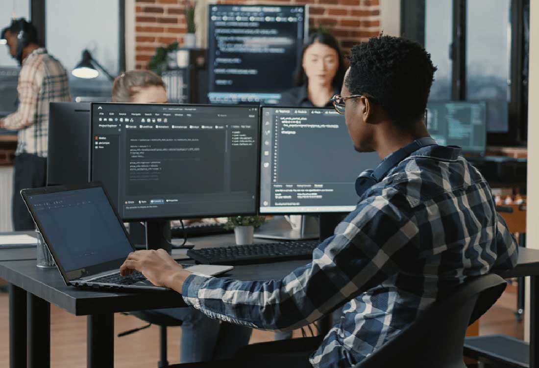 Auburn University at Montgomery computer science student coding at dual monitors in a collaborative campus lab.