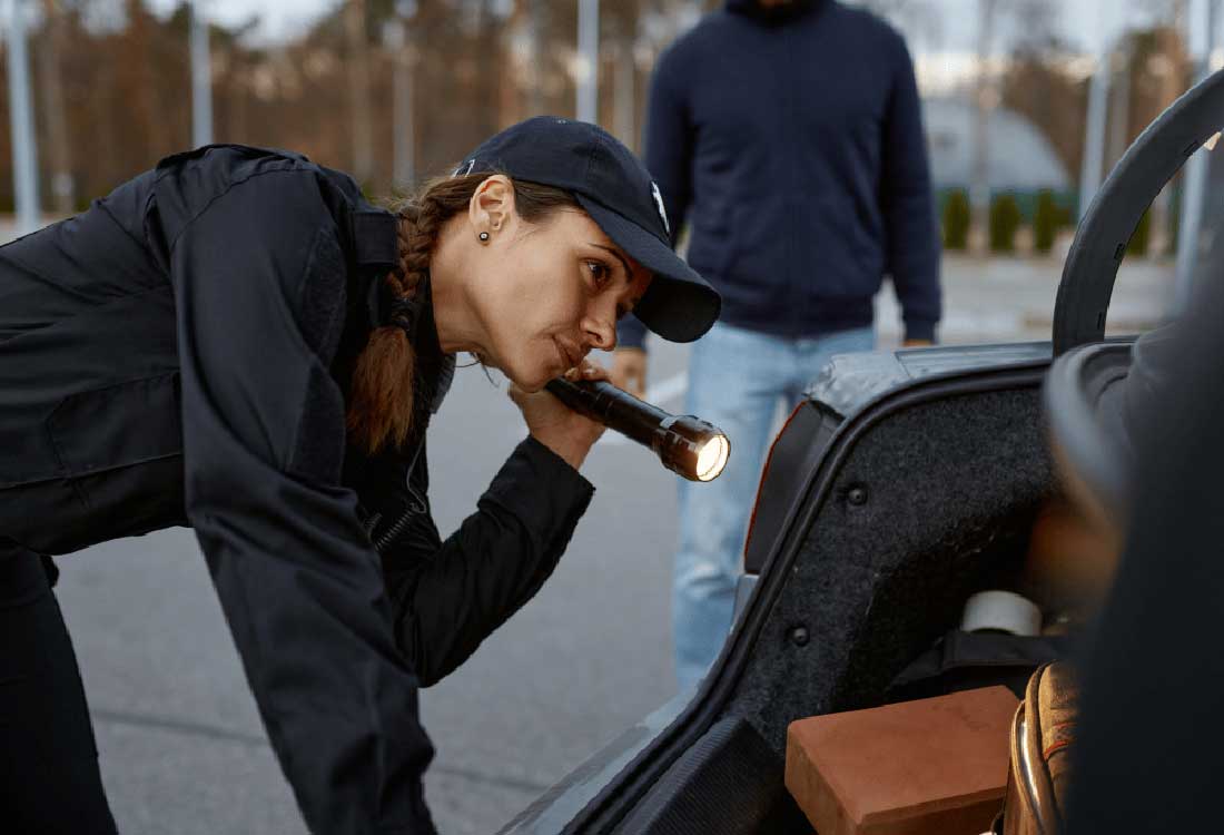 Auburn University at Montgomery criminal justice: a woman in uniform inspects a car trunk with a flashlight