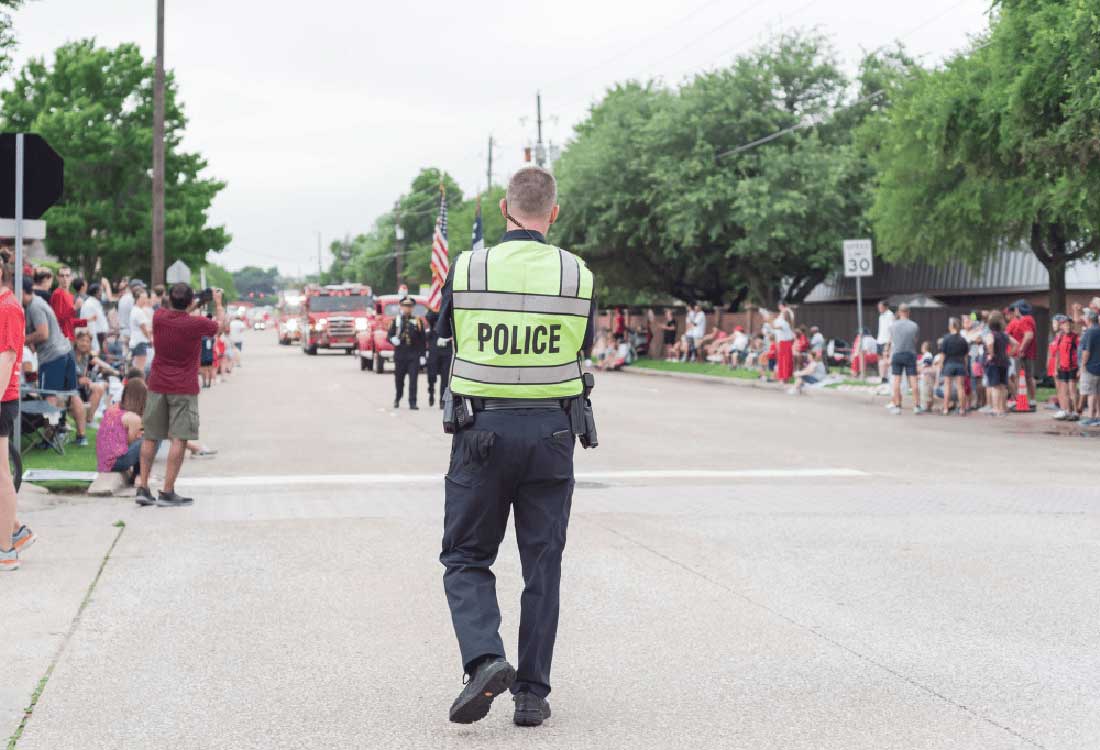 Auburn University at Montgomery police officer directs traffic at community parade with fire trucks, crowds, and flags