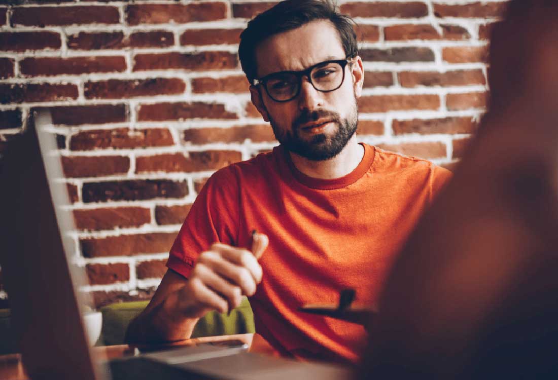 Auburn University at Montgomery student in orange shirt with glasses studying on a laptop in a brick-walled cafe
