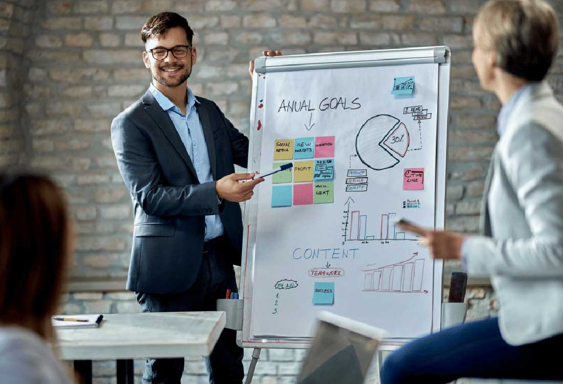 Auburn University at Montgomery AUM business class: a man presents marketing goals on a flip chart to peers.