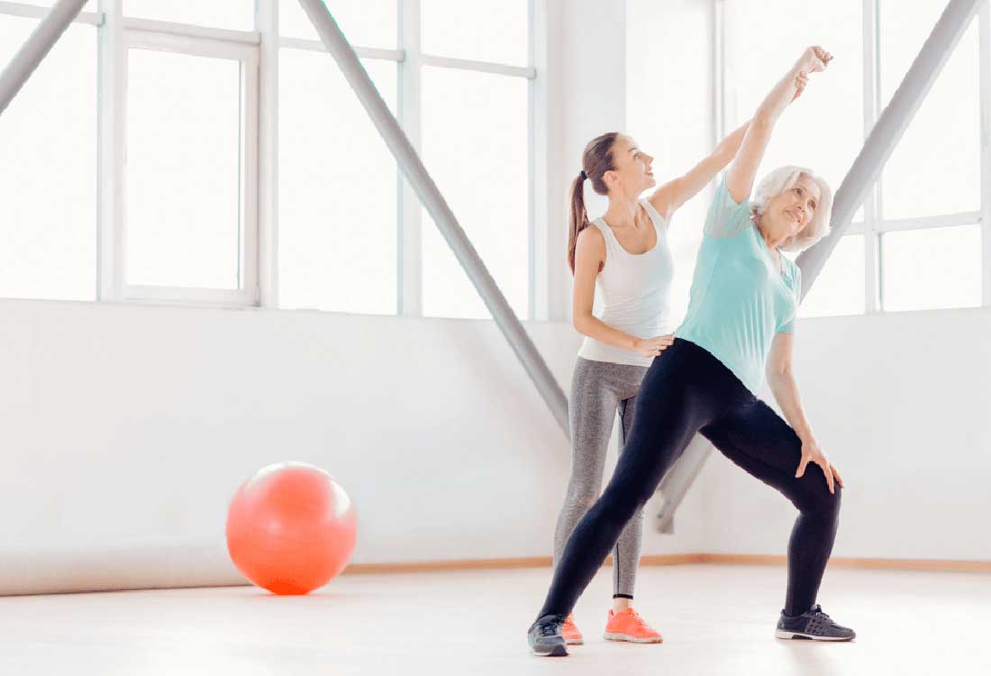 Auburn University at Montgomery trainer assists a woman stretching in a bright fitness studio with an exercise ball