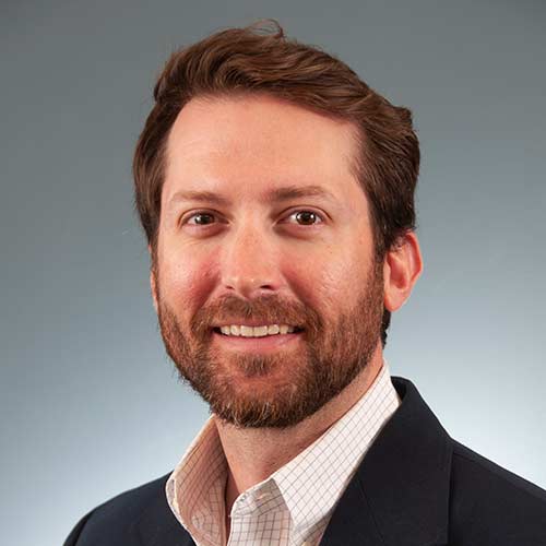 a man wearing a suit and tie smiling at the camera