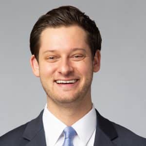 a man wearing a suit and tie smiling at the camera