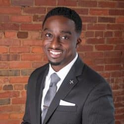 Bambadjan Bamba in a suit standing in front of a brick building