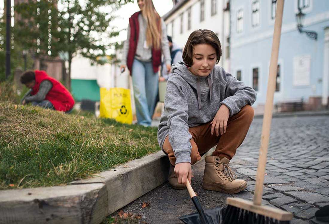 Auburn University at Montgomery students volunteer in a community cleanup, with a student sweeping debris into a dustpan