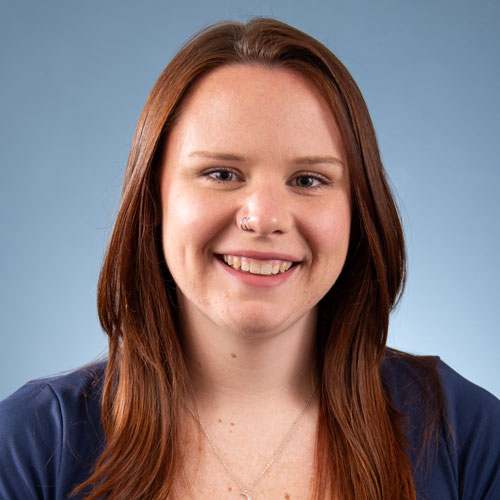 Auburn University at Montgomery headshot of a smiling woman with long red hair on a blue background.