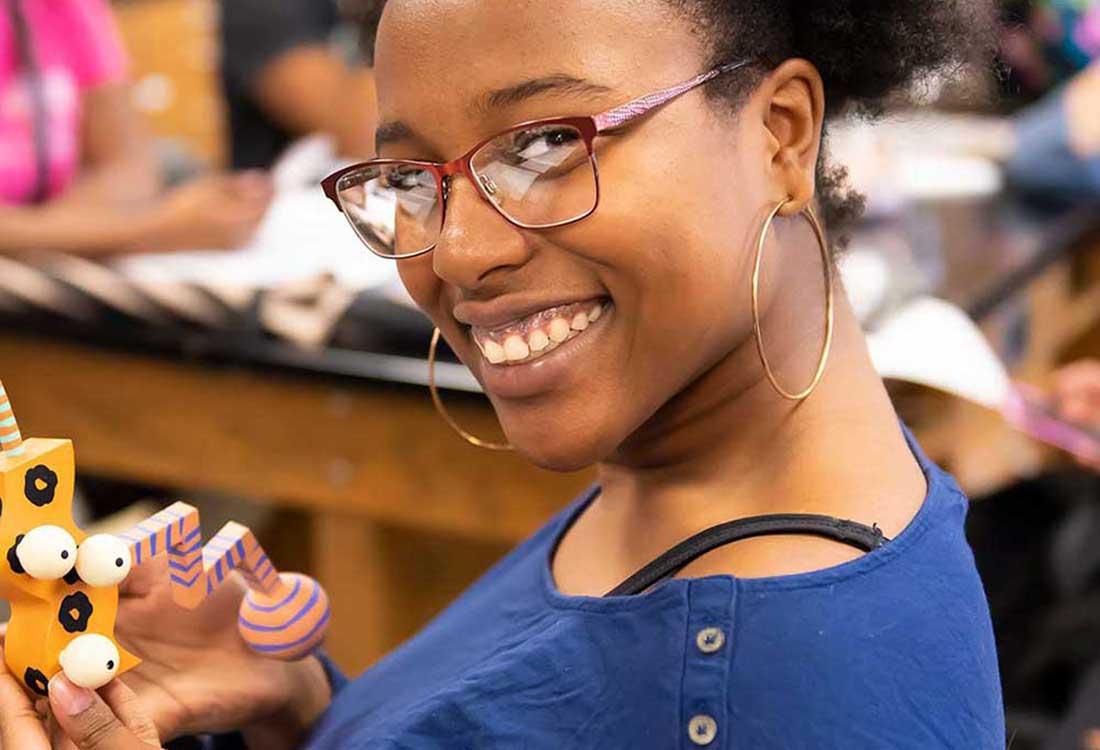 Auburn University at Montgomery art student smiles while holding a colorful sculpture in class