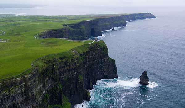 a close up of a hillside next to a body of water with Cliffs of Moher in the background