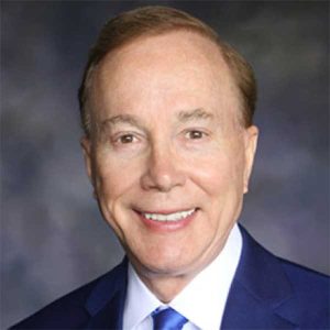 a man wearing a suit and tie smiling at the camera