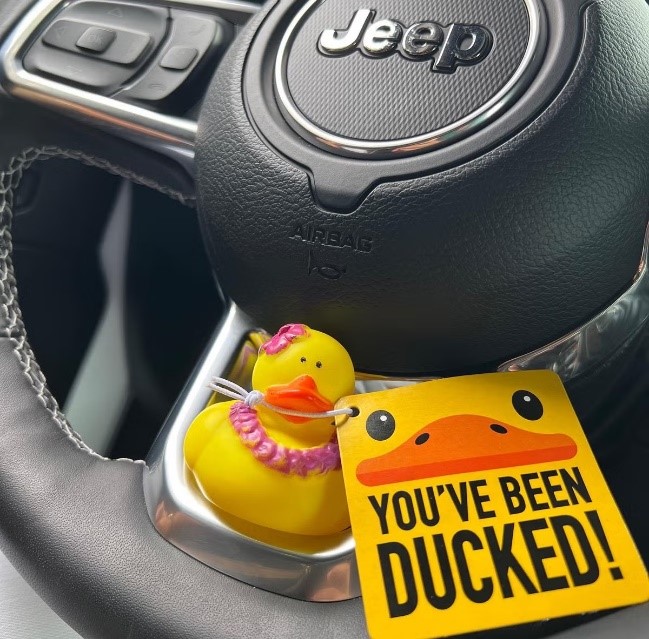 A rubber ducky sits on a Jeep steering wheel with a sign that says, "You've been ducked!"