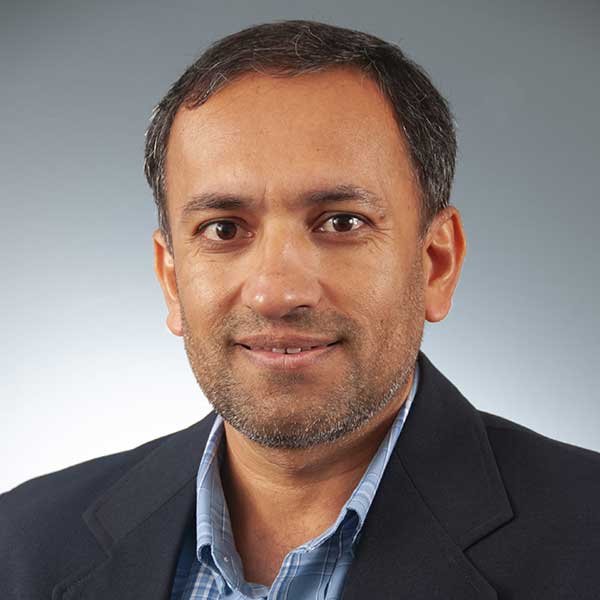 Auburn University at Montgomery faculty member Yolguly Allaberdiyev. Headshot of a man in blazer and blue shirt, smiling against gray background