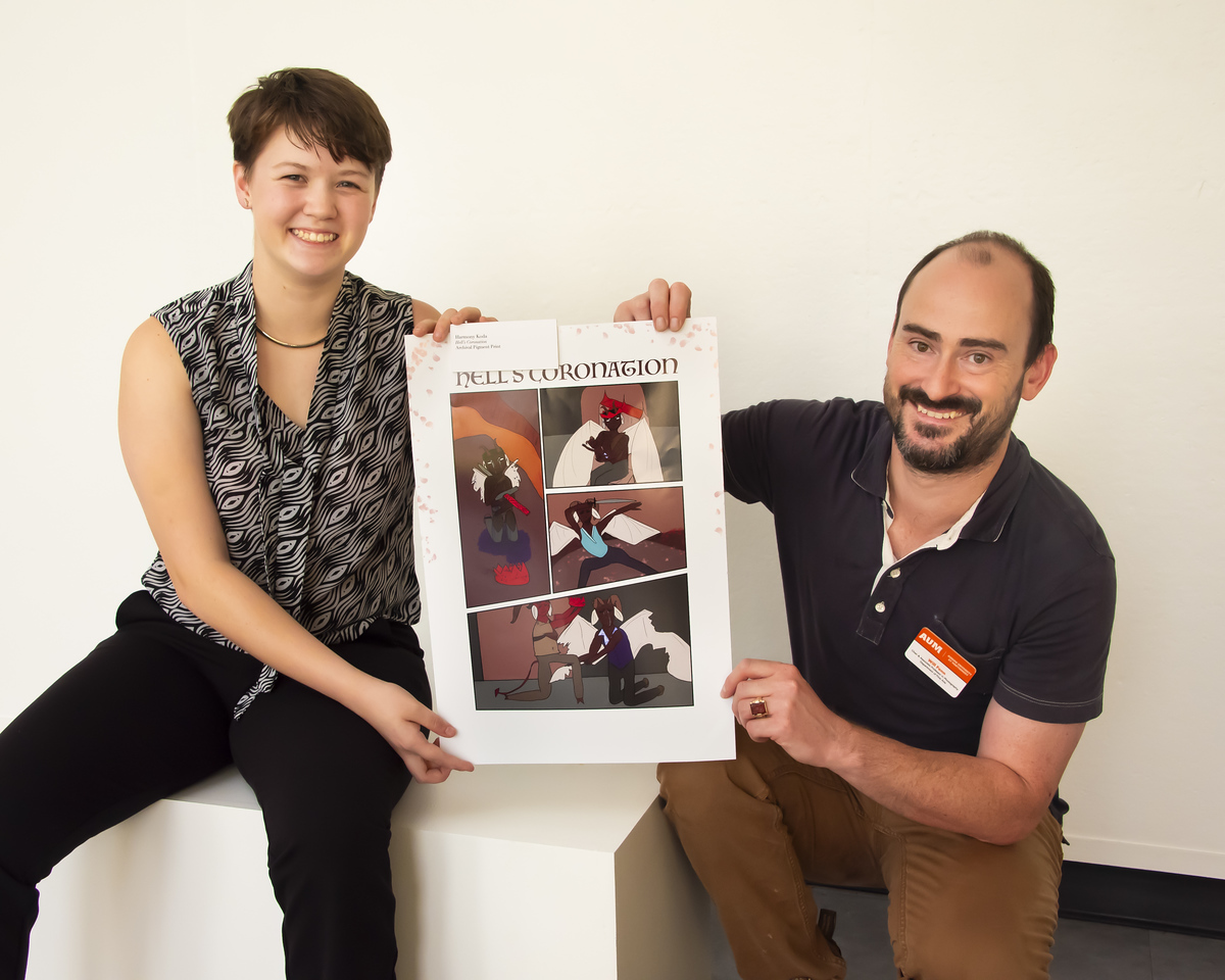 Montgomery area high school student Harmony Koda (left) holds up a printed piece of artwork while Auburn University at Montgomery Department of Fine Arts Chair William Fenn kneeling to the right.