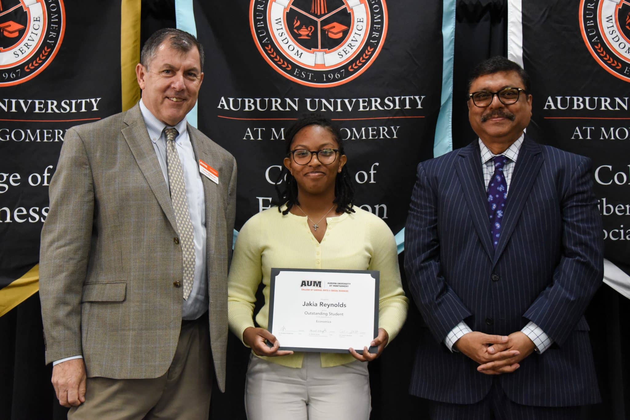 Jakia Reynolds receiving an award at Auburn University at Montgomery event with two men standing beside her.