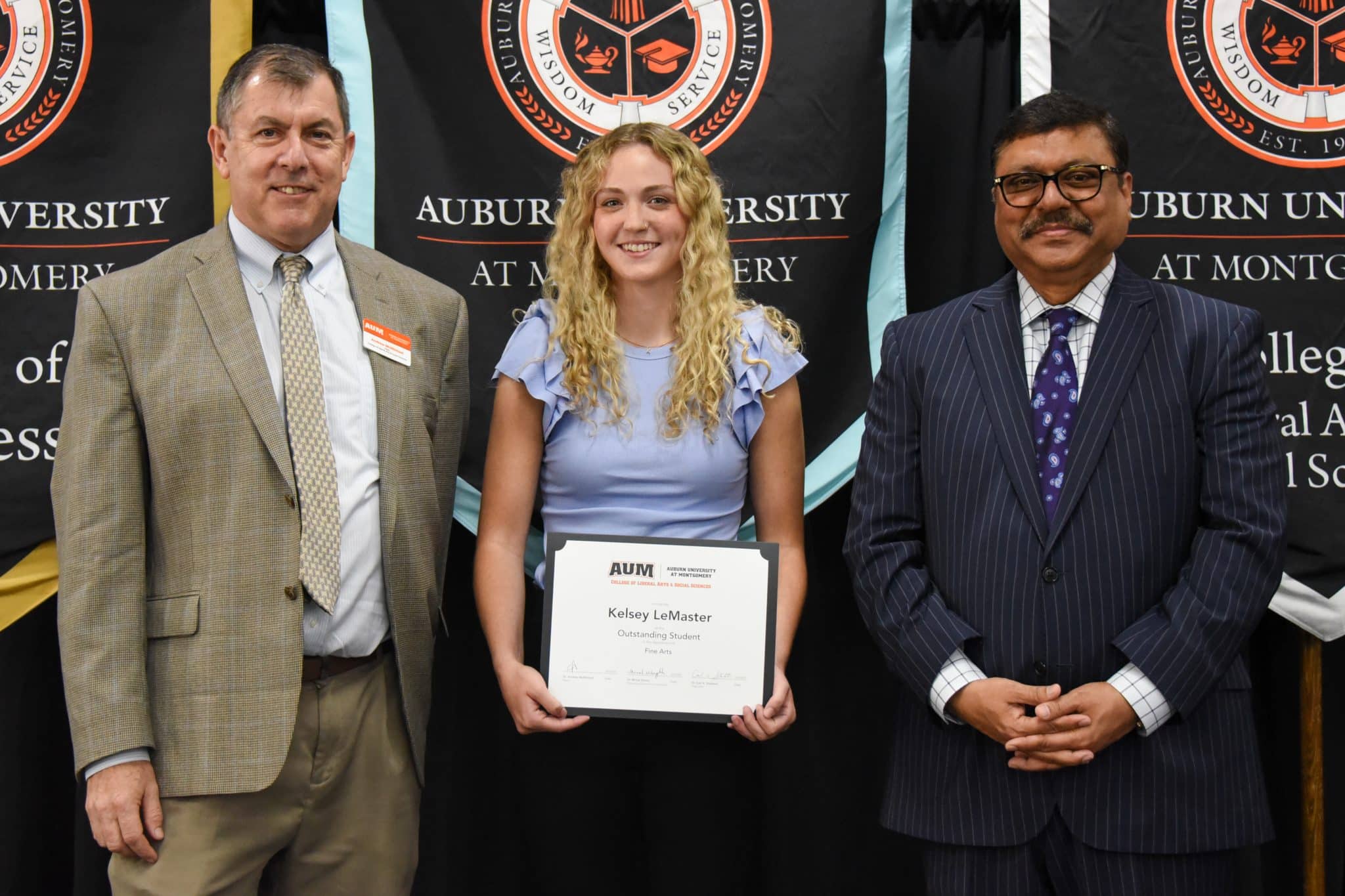 Kelsey LeMaster holds an award certificate at Auburn University at Montgomery ceremony with two men on either side.