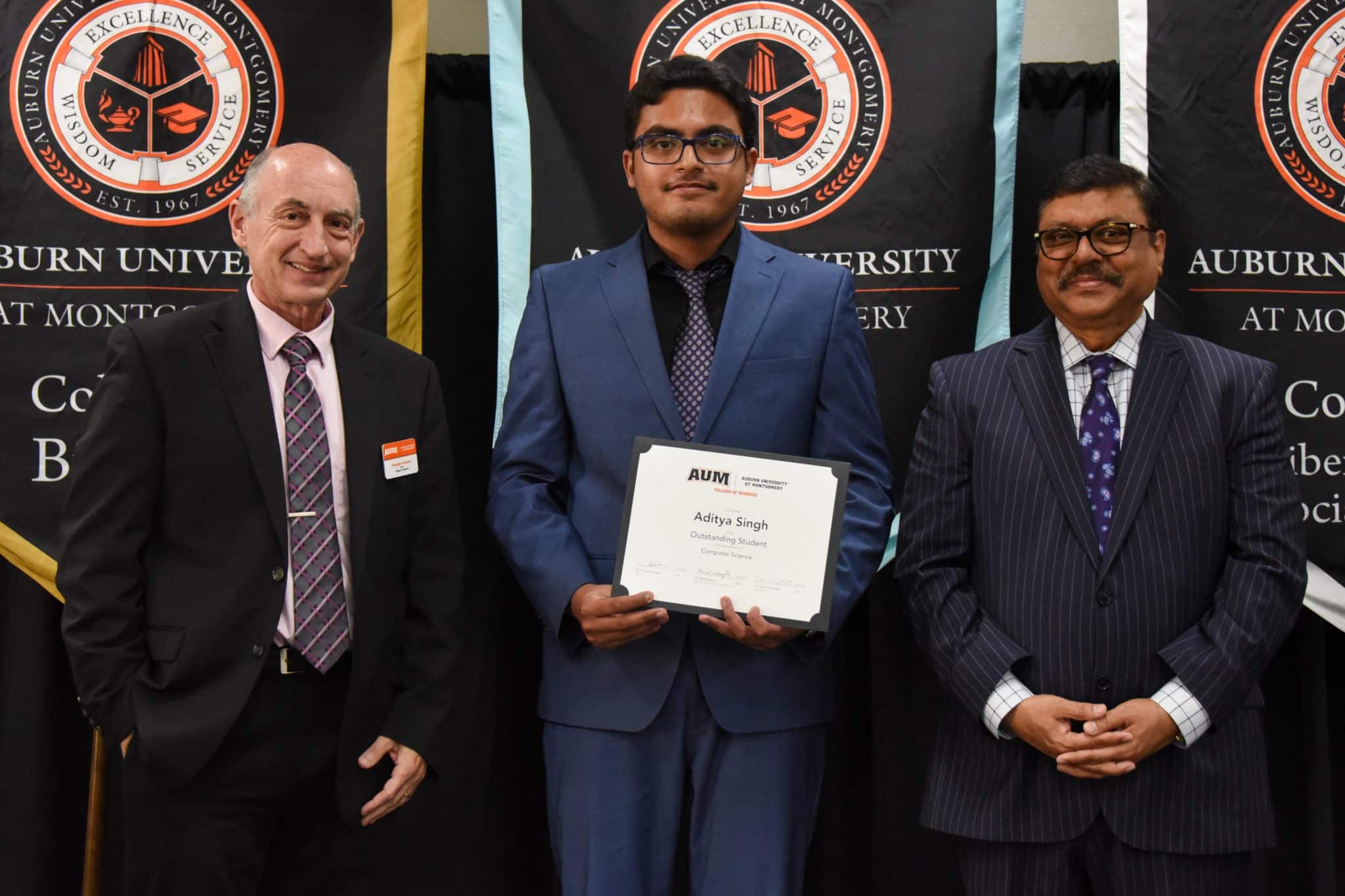 Aditya Singh receives an award at Auburn University at Montgomery ceremony, standing with two men in suits.