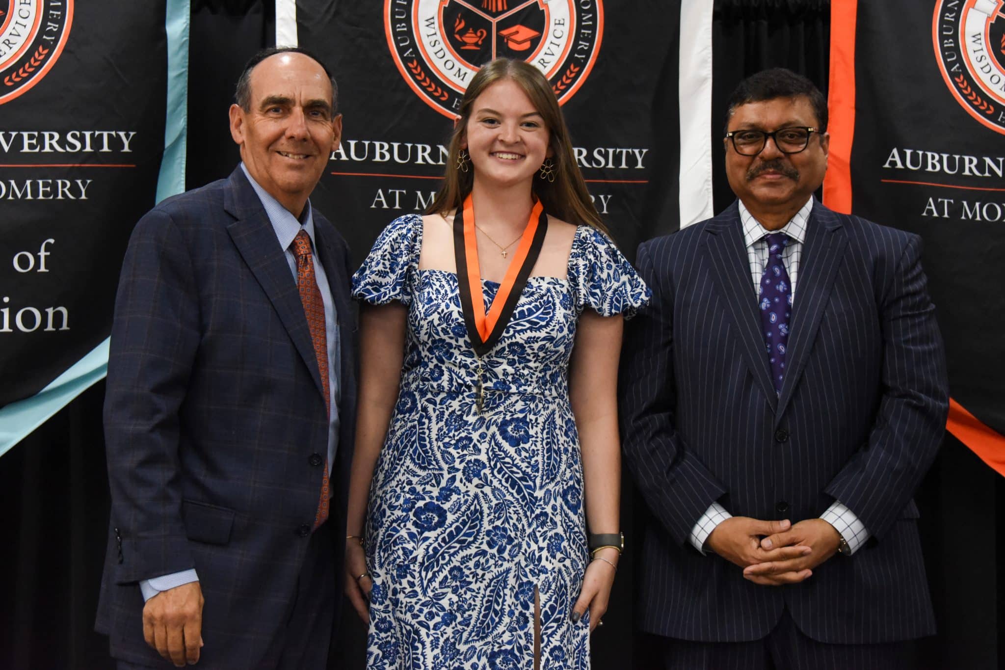 Three people at Auburn University at Montgomery event with banners in background.