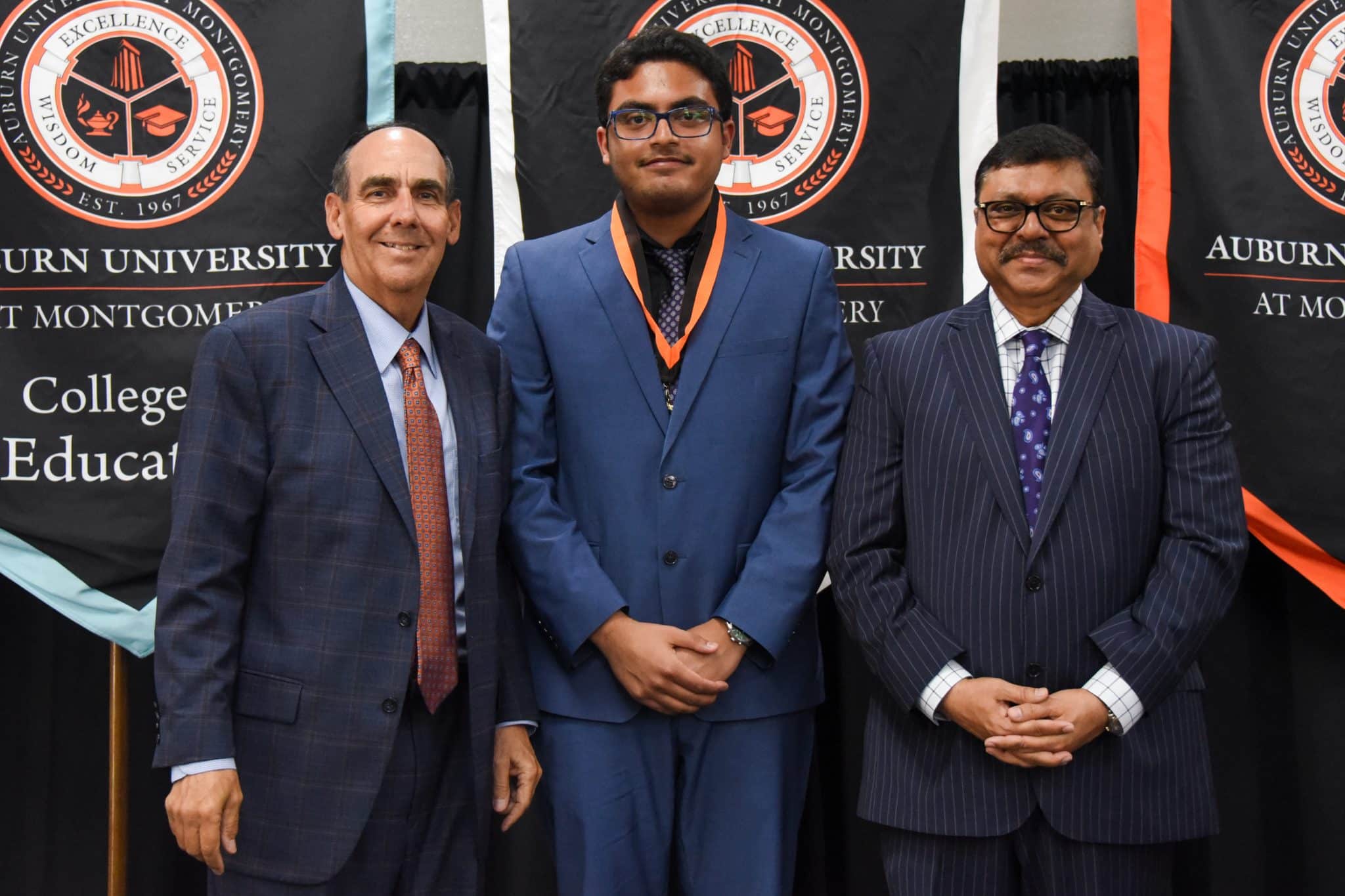 Three men in suits at Auburn University at Montgomery educational event.
