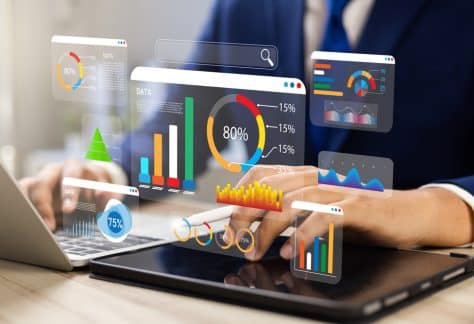 Person analyzing data charts on a tablet and laptop, with floating digital graphs and statistics.