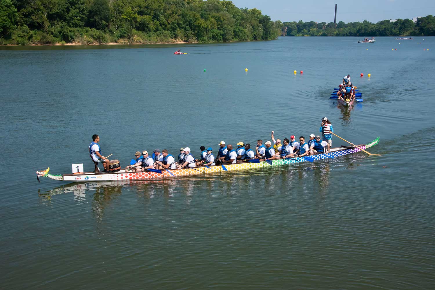 Dragon boat race participants paddle on a calm river under a clear sky.
