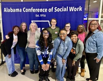 Group of people smiling at Alabama Conference of Social Work banner display.