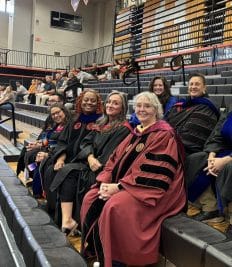 Faculty members in academic regalia seated at a graduation event in an Auburn University at Montgomery gymnasium.