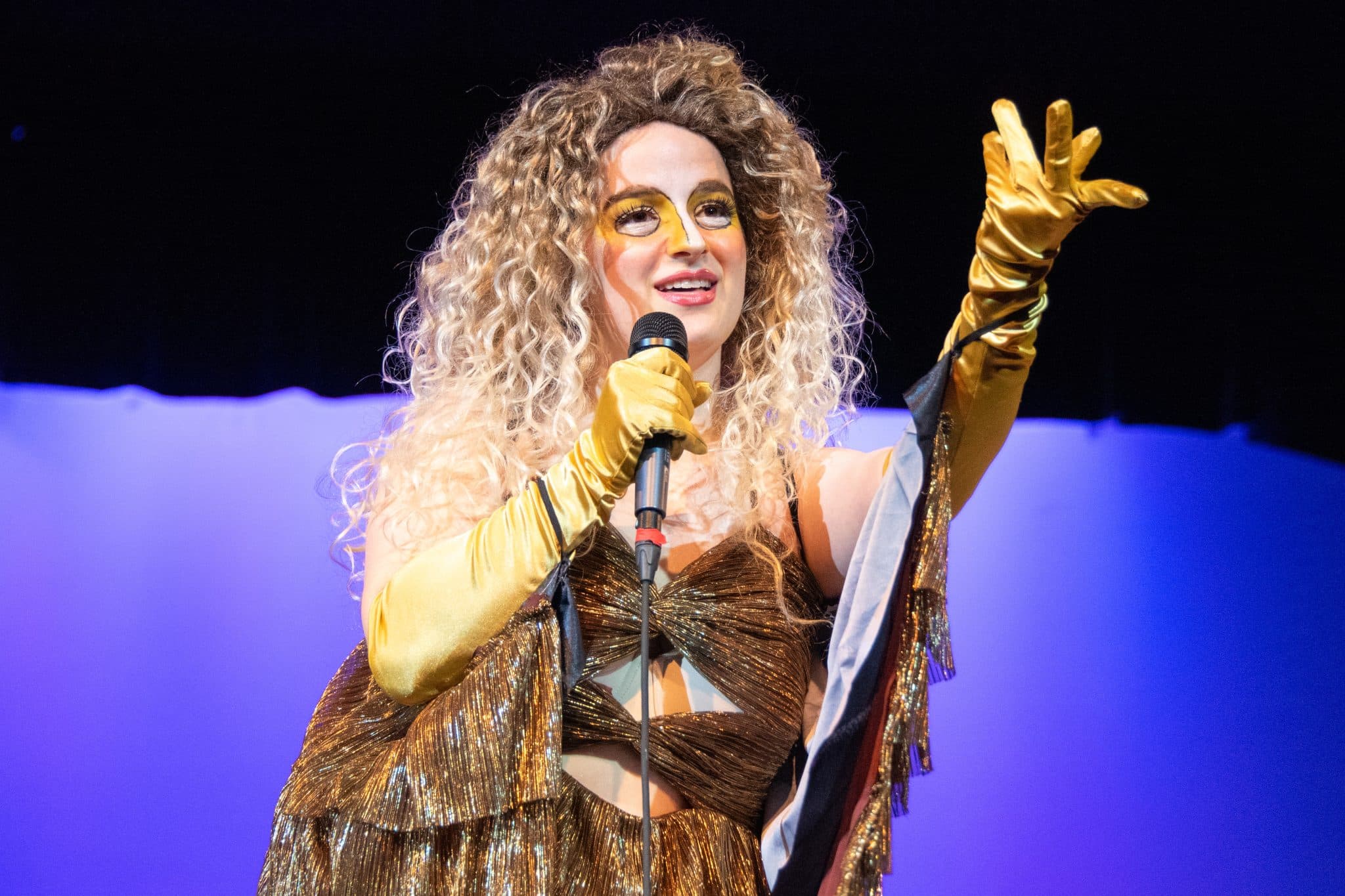 A person in a gold costume and gloves sings into a microphone onstage at Auburn University at Montgomery event.