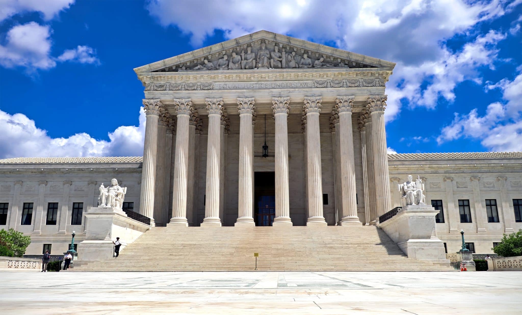 US Supreme Court Building with columns, statues, and blue sky, viewed from the front steps.