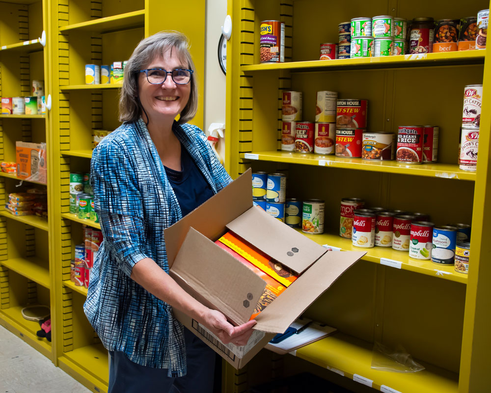 A woman smiling while organizing canned goods in a pantry at Auburn University at Montgomery.