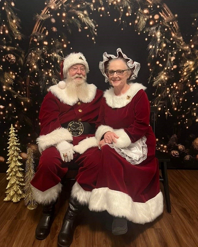 Santa and Mrs. Claus sit together in festive attire with a holiday backdrop.
